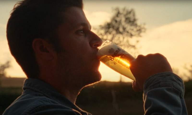 Man neemt een slok Brand pils met de ondergaande zon op de achtergrond